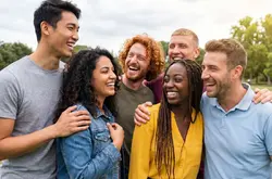Un groupe de six jeunes professionnels rit et partage un moment de complicité en extérieur dans un parc verdoyant. L'ambiance est dynamique, unie et tournée vers la nature.