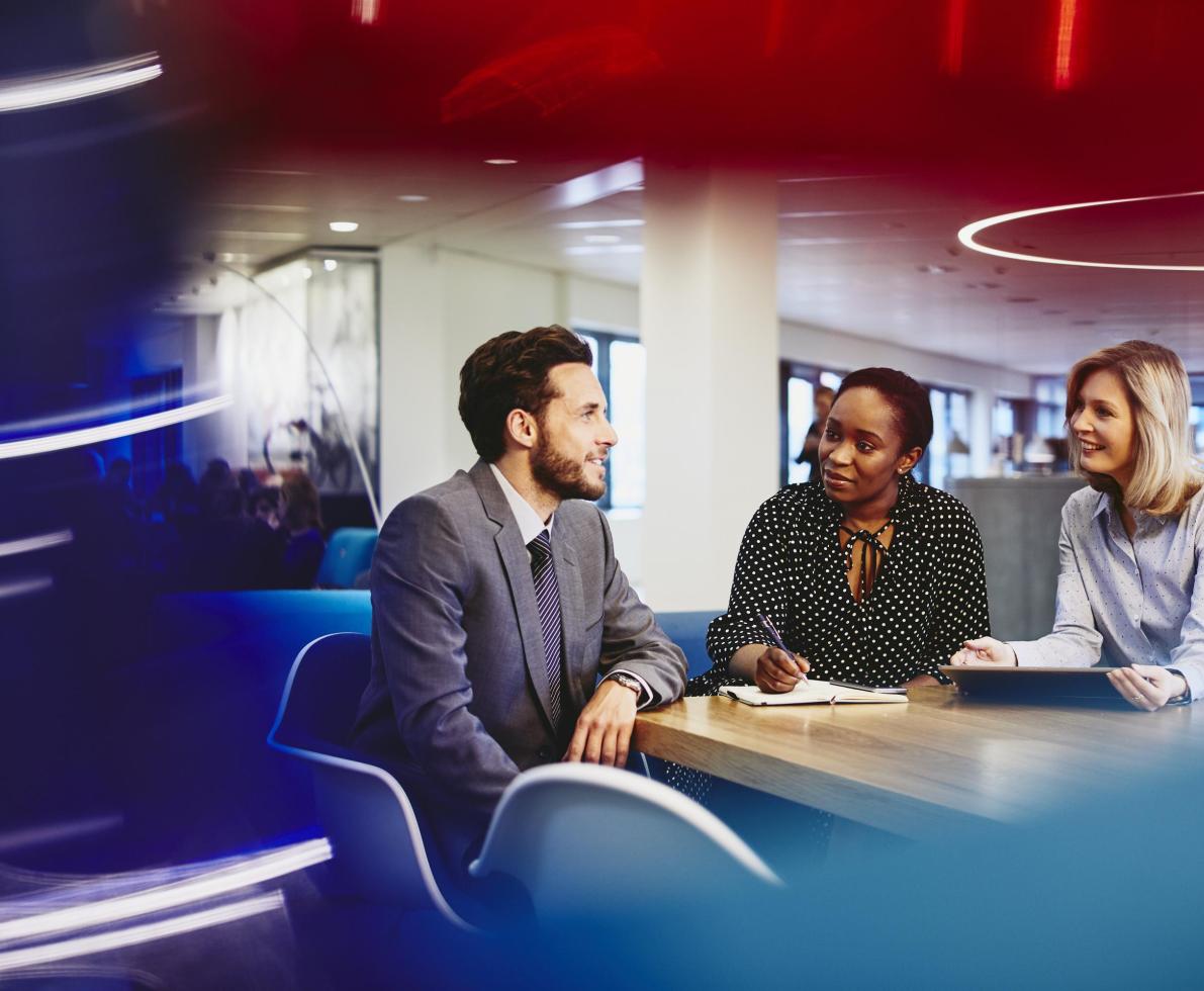 Business man and women in an office having a meeting. Primary colors: blue, red and turquoise.